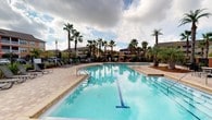 Located at 980 Courthouse Rd, this single-story property is part of a well-appointed community that offers resort-style outdoor amenities in a lush, tropical setting. The centerpiece of the outdoor area is a generously sized swimming pool with clear, blue-tinted water and blue tile lane detailing along the pool floor. The pool features multiple entry points with stainless steel handrails, making it accessible and inviting.

Surrounding the pool is a broad, paved deck finished in warm-toned pavers, providing ample space for lounging. A row of reclining lounge chairs lines one side of the deck, ideal for relaxing in the Florida sun. Tall, mature palm trees are strategically placed throughout the area, offering natural shade and contributing to the tropical ambiance. Additional shaded seating areas with umbrellas are visible in the background, adding to the resort-like atmosphere.

The surrounding community buildings, visible in the backdrop, feature Mediterranean-inspired architecture with warm exterior tones and pitched rooflines. The overall setting is well-maintained and designed to encourage outdoor living, combining functional amenities with a visually appealing, landscaped environment.