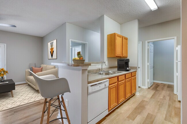 Cocina y comedor en Dunwoody Place con gabinetes de madera clara, electrodomésticos modernos, asientos de barra y líneas de visión abiertas hacia el espacio de estar en un apartamento con ingresos restringidos en Huntsville, Alabama. - Dunwoody Place