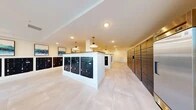 Located at 3701 Southwest 34th Street in Gainesville, Florida, this single-floor mail and package room hallway serves as a central hub for resident mail services. The spacious, open layout is defined by clean white walls and large-format light stone tile flooring that extends throughout, creating a bright and polished aesthetic.

The room features multiple freestanding white-trimmed mailbox islands, each housing rows of black individual mailboxes, complemented by additional wall-mounted mailbox banks lining the perimeter. A dedicated bank of tall parcel lockers along one wall accommodates package deliveries, offering convenient and secure access for residents.

Overhead, a combination of recessed lighting and stylish white pendant lights with brass accents provides warm, even illumination throughout the space. Framed abstract artwork in teal and green tones adds a decorative touch to the walls, softening the utilitarian function of the room.

A connecting hallway features floor-to-ceiling glass panel windows along one side, flooding the corridor with natural light and offering views of the lush outdoor greenery beyond. The overall ambiance is modern and clean, balancing practical functionality with a thoughtfully designed aesthetic that enhances the everyday experience of residents using the space.
