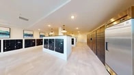 Located at 3701 Southwest 34th Street in Gainesville, Florida, this single-floor mail and package room hallway serves as a central hub for resident mail services. The spacious, open layout is defined by clean white walls and large-format light stone tile flooring that extends throughout, creating a bright and polished aesthetic.

The room features multiple freestanding white-trimmed mailbox islands, each housing rows of black individual mailboxes, complemented by additional wall-mounted mailbox banks lining the perimeter. A dedicated bank of tall parcel lockers along one wall accommodates package deliveries, offering convenient and secure access for residents.

Overhead, a combination of recessed lighting and stylish white pendant lights with brass accents provides warm, even illumination throughout the space. Framed abstract artwork in teal and green tones adds a decorative touch to the walls, softening the utilitarian function of the room.

A connecting hallway features floor-to-ceiling glass panel windows along one side, flooding the corridor with natural light and offering views of the lush outdoor greenery beyond. The overall ambiance is modern and clean, balancing practical functionality with a thoughtfully designed aesthetic that enhances the everyday experience of residents using the space.