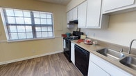 This single-floor residence offers a practical and comfortable living environment with a thoughtfully designed layout. The kitchen serves as a standout feature, showcasing crisp white upper cabinetry that provides ample storage space. Black appliances, including an electric range with overhead ventilation and a dishwasher, lend a clean contrast to the light-toned countertops. A stainless steel sink is positioned conveniently along the counter run, optimizing workflow in the space. Wood-look hard flooring runs throughout, adding warmth and durability underfoot. A window dressed with horizontal blinds allows natural light to filter into the kitchen, brightening the neutral yellow-toned walls and creating an inviting atmosphere. The base trim and overall finishes reflect a clean, well-maintained aesthetic. The single-floor plan ensures easy accessibility and a cohesive flow throughout the home. Overall, the space presents a functional and tidy interior well-suited for everyday living, with key amenities thoughtfully integrated into a compact and efficient footprint.