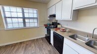 This single-floor residence offers a practical and comfortable living environment with a thoughtfully designed layout. The kitchen serves as a standout feature, showcasing crisp white upper cabinetry that provides ample storage space. Black appliances, including an electric range with overhead ventilation and a dishwasher, lend a clean contrast to the light-toned countertops. A stainless steel sink is positioned conveniently along the counter run, optimizing workflow in the space. Wood-look hard flooring runs throughout, adding warmth and durability underfoot. A window dressed with horizontal blinds allows natural light to filter into the kitchen, brightening the neutral yellow-toned walls and creating an inviting atmosphere. The base trim and overall finishes reflect a clean, well-maintained aesthetic. The single-floor plan ensures easy accessibility and a cohesive flow throughout the home. Overall, the space presents a functional and tidy interior well-suited for everyday living, with key amenities thoughtfully integrated into a compact and efficient footprint.