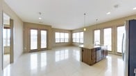 This single-floor space offers an open-concept layout that seamlessly blends the living and kitchen areas into one cohesive, airy environment. Large windows along multiple walls invite an abundance of natural light, creating a bright and welcoming atmosphere throughout the day. A set of glass French doors provides direct access to an outdoor area and further enhances the connection between interior and exterior.

The kitchen is anchored by a substantial dark-wood island topped with granite countertops, complemented by matching cabinetry and stainless steel appliances, including a built-in dishwasher. Pendant lights hang above the island, adding warmth and a modern decorative touch to the culinary space.

Underfoot, large-format, high-gloss white tile flooring stretches across the entire open area, reflecting light and amplifying the sense of spaciousness. The neutral warm-beige walls provide a clean, versatile backdrop that complements the rich tones of the cabinetry and countertops.

Recessed ceiling lighting supplements the natural light, ensuring the space remains well-illuminated at all times. The views through the windows reveal a residential neighborhood, adding context and a sense of community to this bright, functional, and thoughtfully designed living space.