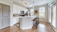 Located at 11 Parklands Dr in Bluffton, SC, this single-story residence offers a thoughtfully designed open layout with consistent hardwood-style flooring flowing through the main living areas. The welcoming entryway hallway leads into the heart of the home, where the kitchen serves as a central hub. It features crisp white cabinetry, a classic subway-tile backsplash, stainless steel appliances including a French door refrigerator, and a large wraparound island with bar seating — illuminated by pendant lighting for a bright, functional atmosphere. Natural light pours in through multiple windows, enhancing the airy, open feel. The living room is generously proportioned, offering outdoor views and ceiling fan overhead, creating a comfortable, relaxed setting. A dedicated dining area provides additional space for entertaining. The bedrooms are carpeted for comfort; one bedroom features large windows with scenic water views, while another includes a walk-in closet. A full bathroom offers a clean, bright vanity with white cabinetry and a mirror, while a second bathroom also provides convenient access. A dedicated in-unit laundry room houses a full-size washer and dryer. Throughout, the neutral color palette and clean finishes contribute to a calm, cohesive living environment well-suited to the coastal Carolina lifestyle.