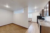 Located at 5730 Leubecher Avenue in Sioux Falls, South Dakota, this efficiently designed single-floor unit makes smart use of its intimate footprint. The open layout connects the kitchen and living area seamlessly, with light wood-tone flooring running through the main spaces and plush carpet in the living and sleeping areas, creating a warm contrast underfoot.

The kitchen is well-appointed with medium-toned wood cabinetry, light countertops, and a full suite of black appliances including a refrigerator, electric range with over-the-range microwave, and dishwasher. A window in the living area allows natural light to filter in, complemented by a wall-mounted HVAC unit for year-round climate control.

The bathroom features a clean, white aesthetic with a full soaking tub and shower combination, a vanity with dark cabinetry, and wood-look flooring for a cohesive finish. White walls throughout the unit keep the space feeling bright and open.

A dedicated laundry area provides added convenience with a stacked washer and dryer unit alongside a water heater, all neatly contained within a separate utility space. Dark wood-toned door frames and baseboards provide subtle definition throughout, giving the unit a polished, cohesive look overall.