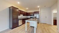 This single-floor residence offers a thoughtfully designed layout that balances functionality and modern style. The kitchen serves as the centerpiece of the space, showcasing rich dark-espresso cabinetry that extends to the ceiling, providing ample storage throughout. Granite countertops run along the perimeter and top the freestanding white kitchen island, creating a striking contrast. A full suite of stainless steel appliances — including a refrigerator with ice maker, built-in microwave, range, and dishwasher — completes the kitchen's professional feel. Light-toned hardwood-style flooring flows throughout the main living and kitchen areas, lending a clean and open ambiance. The bathroom is finished with coordinating dark cabinetry, granite countertops, a single undermount sink, and a full tub-shower combination, all accented by brushed nickel hardware. The bedroom features soft wall-to-wall carpeting, a ceiling fan for year-round comfort, a window that invites natural light and outdoor views, and a walk-in closet with built-in wire shelving for organized storage. Neutral wall tones and recessed lighting throughout contribute to a bright, welcoming atmosphere across the entire residence.