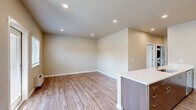 Located at 4040 Hayesville Dr NE in Salem, Oregon, this single-story, three-bedroom, two-bathroom home offers a well-designed layout with modern finishes throughout. The open-concept living and kitchen area serves as the heart of the home, featuring warm-toned luxury vinyl plank flooring, recessed lighting, and a kitchen island with a white countertop. The kitchen is equipped with rich dark wood cabinetry, stainless steel appliances including a refrigerator, range, and over-the-range microwave, making it both functional and visually appealing. Natural light filters in through windows with blinds, complementing the neutral, warm beige wall tones found throughout the home. A wall unit provides climate control in the living area, which also offers direct access to the outdoors. The three bedrooms feature plush carpeting and closets with sliding panel doors, providing ample storage. The primary bedroom is a comfortable size with dedicated closet space. The two bathrooms are clean and practical — one includes a full soaking tub and shower combo with brushed nickel fixtures, while the other features a standalone walk-in shower with sliding glass doors and LVP flooring. A connecting hallway ties the layout together efficiently.
