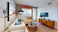 Located at 5805 Charlotte Dr in San Jose, CA, this thoughtfully designed 2-bedroom, 2-bathroom residence offers a well-appointed single-floor layout with a seamless open-concept living and dining area. The kitchen is a standout feature, showcasing rich dark wood cabinetry, quartz countertops, stainless steel appliances, and a peninsula island with pendant lighting overhead — all set atop light hardwood floors that carry throughout the main living areas. The adjacent dining room makes a bold statement with a vibrant orange accent wall, light wood flooring, and a glass-top dining table. The living room offers natural light through large windows with outdoor palm tree views and direct access to a private balcony. The primary bedroom is generously sized, featuring plush carpeting, a ceiling fan, large windows with lush exterior views, and ample closet space. The second bedroom is bright and well-proportioned with soft neutral tones. Both bathrooms are finished with wood-tone cabinetry, quartz vanities, and tub-shower combinations. Additional highlights include in-unit laundry, multiple closets for storage, and two hallways for efficient circulation throughout the home.
