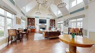 Located at 191 Beach Rd in Salisbury, MA, this single-floor space offers a well-designed, open layout that seamlessly integrates a living room, dining area, and kitchen. The living room serves as a focal point, anchored by a striking floor-to-ceiling stone fireplace with a linear gas insert and a wall-mounted television above the mantle. Rich wood-toned flooring runs throughout, complementing the warm, coastal aesthetic. Adjacent built-in shelving with dark granite countertops provides ample display and storage space, adding a refined, functional touch.

The dining area benefits from an abundance of natural light streaming through large, multi-pane windows that offer views of the surrounding landscape. High ceilings with transom windows amplify the sense of openness and airiness throughout the space. A round pub-style table with wicker-accented chairs creates an inviting spot for casual gathering or dining.

The kitchen is efficiently appointed with rich cherry wood cabinetry, dark granite countertops, a granite tile backsplash, stainless steel appliances, and ample storage. The space is accessed via glass double doors, enhancing connectivity to the exterior. Coastal-inspired décor details, including shell wreaths and sea-toned accents, lend a cohesive, relaxed character to the entire space.