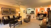 This single-floor residence offers a thoughtfully designed open-concept layout that seamlessly connects the main living areas. The living room serves as the heart of the space, featuring plush carpeted flooring, warm earth-toned walls, and a ceiling fan that adds both style and comfort. The room is well-suited for relaxed gatherings, with ample space for seating arrangements centered around a classic coffee table.

A pass-through counter connects the living area to the kitchen, which is outfitted with white cabinetry extending to the ceiling, a full-size refrigerator, a microwave, and a dark countertop workspace. The kitchen's efficient layout makes it practical for everyday cooking while maintaining a visual connection to the rest of the home.

Adjacent to the living room, a dining area is defined by a bold accent wall in a warm terracotta hue, creating a distinct yet cohesive transition between spaces. The dining space comfortably accommodates a table and chairs, making it ideal for meals or casual entertaining.

Throughout the home, warm lighting and a consistent color palette of cream, brown, and orange tones create an inviting and cohesive ambiance. The overall design balances functionality with comfort, making this a welcoming space for everyday living.