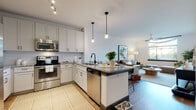 Located at 425 W Trade St in Charlotte, NC, this single-floor residence offers a thoughtfully designed open-concept layout that seamlessly connects the kitchen, dining, and living areas. The kitchen is a standout feature, boasting white shaker cabinetry, granite countertops, a large center island with pendant lighting, and a full suite of stainless steel appliances including a refrigerator, range, built-in microwave, and dishwasher. The space flows naturally into the living room, where large windows invite abundant natural light and offer outdoor views, complemented by a ceiling fan and wood-style flooring throughout. The living area provides a comfortable and versatile setting with clean, neutral walls that enhance the bright, airy ambiance. The bedrooms are generously sized, each featuring wood-style flooring, ample natural light from well-positioned windows, and access to closet storage. The bathroom is finished with granite-topped vanity cabinetry, large-format tile flooring, subway tile surrounds in the tub/shower combination, and a distinctive louvered storage door. Throughout the residence, a cohesive modern aesthetic is maintained with crisp white walls, dark accent hardware, and warm wood tones that create an inviting, contemporary urban living experience.
