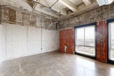 Located at 1 Hermann Park Court in Houston's Medical Center area, this one-bedroom, one-bathroom loft showcases a distinctive industrial aesthetic throughout its single floor. The living area makes a bold architectural statement with exposed concrete walls, raw brick masonry accents, and an open ceiling revealing structural beams, ductwork, and conduit — all hallmarks of authentic loft-style design. Polished concrete floors run continuously throughout, reinforcing the industrial character while reflecting natural light that enters through large windows offering elevated city views.

The kitchen is well-appointed with rich wood cabinetry, granite countertops, a tile backsplash, stainless steel appliances including a refrigerator and dishwasher, and a double-basin sink. Track lighting above the kitchen adds functional illumination while complementing the loft's urban aesthetic.

The bedroom features white walls that contrast with exposed concrete, a dedicated closet, and a window framing outdoor views. A hallway connects to the full bathroom, which includes a soaking tub and shower combination with classic white tile and a bold navy accent stripe, a dark wood vanity with granite countertop, and a built-in sink. A utility room with in-unit laundry completes this efficiently designed urban residence.