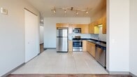 Located in the heart of Grand Rapids, MI, Unit 1201 at 10 Commerce Ave SW offers a thoughtfully designed single-floor layout that maximizes every square foot. The entryway hallway features clean white walls, recessed lighting, and warm wood-look flooring that carries throughout the main living areas, creating a cohesive and inviting atmosphere.

The kitchen is a standout feature, outfitted with warm maple cabinetry, dark granite countertops, and a full suite of stainless steel appliances including a refrigerator, range, microwave, and dishwasher. Large-format light tile flooring grounds the kitchen space, while a curved track lighting fixture overhead provides bright, directed illumination. The layout is efficient and functional, offering ample cabinet storage and counter workspace.

The unit includes two bathrooms. The first is a well-appointed full bath featuring a glass-enclosed walk-in shower with large-format neutral tile, a built-in bench, and modern chrome fixtures. The second bathroom offers a dark granite vanity top with an undermount sink, a large mirror, and accessibility-friendly grab bars throughout. Both bathrooms are finished with light tile flooring for a clean, modern look.

Throughout the unit, the contrast of wood-look flooring in living areas and tile in the kitchen and bathrooms adds visual interest, while the neutral color palette keeps the space feeling bright and open.