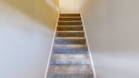 Located at 4441 E Honeygrove Ct in Virginia Beach, VA, this two-story home offers three bedrooms, two bathrooms, and a well-organized layout across its two levels. Carpeted stairs with white-painted risers connect the floors, lending a clean, classic aesthetic throughout.

The upper level hosts the main living areas, including a combined dining and living room with plush carpeting, neutral walls, and a decorative white railing that overlooks the staircase. The kitchen is thoughtfully updated with white shaker-style cabinetry, white quartz countertops, stainless steel appliances — including a refrigerator, electric range, and dishwasher — and warm hardwood-style flooring. A window above the sink brings in natural light.

The three bedrooms are carpeted and finished in soft neutral tones, each offering closet space with bi-fold louvered doors. The spacious primary bedroom features dual windows that invite natural light. Both bathrooms are appointed with elegant marble-look tile surrounds on the tub-shower combinations, built-in niche shelving, white vanities, and hardwood-style flooring, providing a refined and cohesive finish. A dedicated laundry area and multiple closets add practical storage throughout this well-appointed Virginia Beach home.