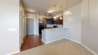 This single-floor residence offers a thoughtfully designed open-concept layout that connects the kitchen and living area seamlessly. The kitchen is well-equipped with rich dark cabinetry, granite-style countertops, black appliances including a range, microwave, and refrigerator, and a double stainless steel sink. A peninsula with pendant lighting overhead defines the transition into the living area, which features plush wall-to-wall carpeting, a ceiling fan, and a window with blinds that draws in natural light.

The bedrooms are carpeted and finished in neutral tones, with one room offering vaulted ceiling details and access to a walk-in closet outfitted with a full-width shelf and hanging rod. The bathroom includes a dark vanity with granite-style countertops, a large mirror, and stone-look tile flooring. A dedicated laundry space houses a full-size washer and dryer side by side, along with a water heater and overhead shelving. Throughout, six-panel doors, consistent neutral wall tones, and wood-look flooring in the kitchen tie the design together cohesively.