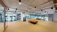 Located at 1315 Adams Street in Nashville, Tennessee, this two-floor fitness facility offers an impressive amount of dedicated exercise space spread across both levels. The larger main floor provides an expansive workout environment, while the upper level offers additional training area accessible via an open-riser staircase with metal railings that serves as both a functional and architectural element.

The facility features an industrial-modern aesthetic throughout, with exposed concrete ceilings, visible ductwork and piping, and pendant lighting lending a raw yet refined character to the space. Rubber-cushioned flooring covers both levels, providing comfort and durability underfoot across all training zones.

The main floor is generously equipped with rows of treadmills, cable machines, selectorized strength equipment, plate-loaded machines, and free weights including a full dumbbell rack with medicine balls. A spacious open-floor area with mirrored walls is ideal for functional training and stretching. The upper level houses additional cardio equipment, including stationary bikes and stair climbers, and benefits from floor-to-ceiling glass windows that flood the space with natural light and offer views of the surrounding Nashville neighborhood. The combination of scale, equipment variety, and thoughtful design makes this a well-appointed, high-capacity fitness destination.