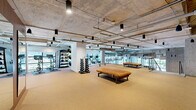 Located at 1315 Adams Street in Nashville, Tennessee, this two-floor fitness facility offers an impressive amount of dedicated exercise space spread across both levels. The larger main floor provides an expansive workout environment, while the upper level offers additional training area accessible via an open-riser staircase with metal railings that serves as both a functional and architectural element.

The facility features an industrial-modern aesthetic throughout, with exposed concrete ceilings, visible ductwork and piping, and pendant lighting lending a raw yet refined character to the space. Rubber-cushioned flooring covers both levels, providing comfort and durability underfoot across all training zones.

The main floor is generously equipped with rows of treadmills, cable machines, selectorized strength equipment, plate-loaded machines, and free weights including a full dumbbell rack with medicine balls. A spacious open-floor area with mirrored walls is ideal for functional training and stretching. The upper level houses additional cardio equipment, including stationary bikes and stair climbers, and benefits from floor-to-ceiling glass windows that flood the space with natural light and offer views of the surrounding Nashville neighborhood. The combination of scale, equipment variety, and thoughtful design makes this a well-appointed, high-capacity fitness destination.