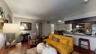 This single-story residence offers a well-organized layout connecting multiple living spaces through arched entryways and an open flow. The living room serves as the central gathering area, featuring rich hardwood-style flooring, a textured ceiling, and generous wall space. An arched passageway connects the living area to additional rooms, lending architectural character to the interior.

The galley-style kitchen is outfitted with dark espresso cabinetry, granite-style countertops, a tile mosaic backsplash, and black appliances including a range, microwave, and refrigerator. A breakfast bar-style counter opening connects the kitchen to the adjacent dining area, which accommodates a full dining set.

Two bedrooms are carpeted for comfort, each featuring windows with blinds that allow natural light, textured ceilings, and ample space for standard bedroom furnishings. One bedroom offers a direct sightline to the living area through an open doorway.

Two bathrooms serve the unit. One features a dark-stained vanity with a granite-style countertop and a separate water closet. The second includes a full bathtub with a shower and hardwood-style flooring, completing the functional layout of this well-appointed residence.