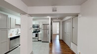 This efficient and thoughtfully designed 1-bedroom, 1-bathroom unit offers a clean, modern aesthetic throughout its single-floor layout. Warm, rich hardwood-style flooring flows through the living areas, hallway, and bedroom, creating a cohesive and inviting atmosphere, while light tile flooring defines the kitchen space.

The combined kitchen and living area serves as the heart of the unit. The kitchen is well-equipped with a full suite of stainless steel appliances, including a refrigerator, range, microwave, and dishwasher, complemented by white shaker-style cabinetry and light countertops. Natural light filters into the living area through large windows dressed with white horizontal blinds, offering views of surrounding greenery.

The bedroom is a comfortable, well-lit retreat featuring two windows that bring in ample natural light and views of the outdoors. A dedicated closet provides convenient storage. The bathroom is finished with classic white subway tile in the walk-in shower with a sliding glass door, neutral floor tile, and built-in shelving for added practicality.

A private entryway with a secure door, a dedicated closet, and a central HVAC system round out the functional features of this tidy, move-in-ready unit.