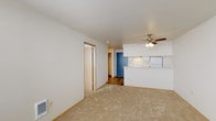 This single-floor residential unit offers a practical and straightforward layout designed for comfortable everyday living. The living area is carpeted in neutral tones and features a ceiling fan with integrated lighting, creating a bright and airy atmosphere. A wall-mounted heater provides efficient climate control, and the open sightlines connect the living space seamlessly to the kitchen area.

The kitchen is equipped with white cabinetry, a coil-burner electric range, a refrigerator, and a countertop peninsula that serves as a natural divider between the kitchen and living space. The flooring in the kitchen and hallway transitions to wood-look vinyl planking, adding warmth and durability to the high-traffic areas. Under-cabinet lighting and ample upper storage enhance the kitchen's functionality.

A hallway leads from the kitchen to the bedroom and bathroom, offering a clear and efficient flow throughout the unit. The bedroom is generously sized, carpeted, and features a window with horizontal blinds that allow for natural light and privacy. A baseboard heater ensures consistent warmth in the room.

The bathroom is clean and well-appointed, featuring a single-sink vanity with white cabinetry, a large mirror with overhead lighting, wood-look flooring, and a full-size soaking tub and shower combination with white surround panels. A closet with sliding doors provides additional storage near the bedroom.