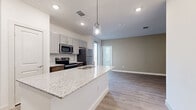This single-story unit offers four bedrooms and two bathrooms within a thoughtfully designed floor plan. The open-concept kitchen and living area serves as the central hub of the space, featuring light wood-look flooring, recessed lighting, and a ceiling fan. The kitchen is well-appointed with gray shaker-style cabinetry, stainless steel appliances including a refrigerator, range, and microwave, and a granite-topped island with a double sink and pendant lighting above. The kitchen flows seamlessly into the living area, which features warm, neutral-toned walls and access to natural light through windows near the entry.

The four bedrooms are carpeted and finished with clean white walls, providing a neutral and comfortable atmosphere. Each room includes panel-style doors, and select bedrooms feature windows with blinds for natural light. One closet serves the unit for additional storage needs.

Both bathrooms are finished consistently with wood-look tile flooring, gray vanities topped with granite counters, and tub-shower combinations with white subway tile surrounds and brushed nickel fixtures. The overall design is clean, contemporary, and cohesive throughout.