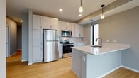 This single-floor space showcases a contemporary design with a cohesive neutral color palette throughout. The kitchen serves as a central highlight, featuring white shaker-style cabinetry with matte black hardware, crisp white quartz countertops, and a classic subway tile backsplash. Stainless steel appliances, including a French door refrigerator, electric range with over-the-range microwave, and dishwasher, provide a polished, functional finish. A peninsula island with an integrated sink and pendant lighting above adds both prep space and a casual gathering area. Light hardwood flooring runs throughout the kitchen and living areas, complementing the warm, neutral wall tones.

The bathroom is finished with large-format dark tile flooring, a white vanity with quartz countertop, and a full tub-shower combination with built-in shelving. Neutral gray walls create a clean, understated aesthetic.

The bedrooms feature plush wall-to-wall carpeting and soft gray walls, with windows allowing natural light to fill each room. The 3D floor plan reveals a well-organized layout with clearly defined living, sleeping, and utility zones, ensuring efficient use of the available space throughout.