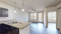 This single-floor residence showcases a thoughtfully designed open-concept layout, where the kitchen flows seamlessly into the living area. The kitchen is equipped with dark espresso cabinetry, black appliances, and a granite-topped peninsula island with an undermount sink. Pendant lighting hangs above the island, providing focused task lighting that complements the overall bright and neutral palette.

Hardwood-style flooring in a cool gray tone runs consistently throughout the entire space, contributing to a cohesive and modern aesthetic. Crown molding adds a refined architectural detail to the living area, which features a ceiling fan and windows paired with a glass-panel exterior door, allowing abundant natural light and outdoor access.

The bedrooms are well-proportioned, each featuring hardwood-style flooring, blinds-fitted windows, and ceiling fans where applicable. Rooms are finished with clean white walls and panel-style interior doors, maintaining a uniform, polished feel.

The bathroom includes a granite-topped vanity with dark cabinetry, consistent with the kitchen's design language. Notably, a spacious walk-in closet with built-in shelving and hanging rods adjoins the bathroom, offering considerable storage capacity. Additional built-in shelving is visible in other areas of the unit, further enhancing functional storage throughout the space.
