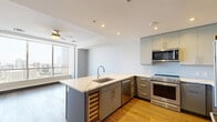 Located in the heart of downtown Dallas on Pacific Avenue, this modern one-bedroom, one-bathroom residence offers a thoughtfully designed open layout with high-end finishes throughout. Floor-to-ceiling windows flood the living area with natural light and frame breathtaking panoramic views of the Dallas skyline, including the iconic Bank of America Plaza.

The open-plan kitchen and living area is anchored by a sleek kitchen featuring a large island with a quartz waterfall countertop, an undermount sink, and stainless steel appliances including a French door refrigerator, range, and built-in microwave. Grey cabinetry with modern hardware and a subway tile backsplash complete the contemporary aesthetic, while warm hardwood flooring runs throughout the main living spaces.

The spacious bedroom is finished with plush carpet and large windows that continue the stunning city views. A dedicated walk-in closet offers built-in shelving and hanging rails for ample storage. The full bathroom is elegantly appointed with large-format tile flooring, a glass-enclosed walk-in shower with stone tile surround, recessed niche, and a rainfall showerhead. The overall ambiance is clean, modern, and urban—ideal for sophisticated city living.
