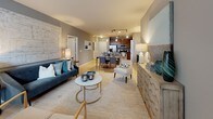 This single-floor residence offers a thoughtfully designed open-concept layout that seamlessly connects the living, dining, and kitchen areas. Light hardwood-style flooring runs throughout the main living spaces, complementing the neutral gray walls and creating a bright, cohesive atmosphere. The living area is generously proportioned, with large windows dressed in sheer curtains that invite natural light and provide outdoor views.

The kitchen is a standout feature, showcasing rich dark wood cabinetry, dark granite countertops, stainless steel appliances including a gas range and French door refrigerator, and a peninsula with bar seating. Track lighting overhead enhances both functionality and ambiance. A built-in pantry with open shelving adds practical storage.

The bedrooms are carpeted for comfort and feature teal accent walls, ceiling fans, and windows with outdoor views. The primary bedroom connects to a well-appointed en suite bathroom with dark granite countertops, wood cabinetry, tile flooring, and access to a walk-in closet. A secondary bathroom mirrors the same finishes, offering a tub-shower combination. Throughout, the design maintains a consistent, contemporary aesthetic with warm tones and quality materials.