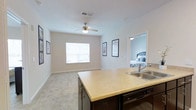This single-floor residence showcases an open-concept layout that seamlessly connects the kitchen and living area, creating a cohesive and functional living space. The kitchen features a dark-cabinetry island with a light-toned countertop and a stainless steel double sink, complemented by a dishwasher integrated beneath the island. The design allows for easy interaction between the kitchen and the adjoining living area.

The living space is finished with neutral-toned carpet and is illuminated by a ceiling fan with a built-in light fixture, providing both comfort and airflow. A window along the far wall invites natural light into the room, brightening the open area. The walls are painted in a soft, neutral tone, contributing to a clean and welcoming ambiance throughout.

Framed artwork adorns the living room walls, adding a decorative touch to the space. A doorway visible from the main living area leads into a bedroom, which features its own overhead lighting and continues the neutral color palette. The overall layout is practical and well-connected, offering a comfortable and cohesive living environment.