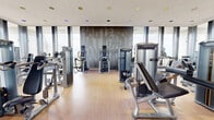 Located at 800 Main St in Hartford, CT, this fitness center offers a well-appointed, two-room exercise facility designed for a comprehensive workout experience. The space is defined by dramatic floor-to-ceiling windows that wrap around the main exercise room, flooding the area with natural light and framing expansive views of the Hartford skyline and beyond — a standout feature that elevates the overall ambiance.

The primary exercise room is generously sized and outfitted with a full suite of professional-grade Matrix cardio and strength equipment, including treadmills, ellipticals, cable machines, and a variety of selectorized weight stations. Light hardwood-style flooring runs throughout, complementing the modern, warm-toned wood accent wall that bears a decorative emblem — adding a refined, upscale character to the space. Recessed ceiling lighting provides even illumination throughout.

The secondary exercise room offers a more intimate setting, featuring additional strength equipment, a recumbent bike, and open floor space with an exercise mat, ideal for stretching or functional training. Rich wood-paneled walls and large windows continue the design language of the main room.

A dedicated entry and transition area includes rubberized flooring, a water fountain station, a flat bench, and convenient access between the two rooms, rounding out this well-equipped fitness facility.
