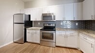 This 800-square-foot, one-bedroom, two-bathroom residence at 2054 Riverside Avenue in Jacksonville, Florida, delivers a well-appointed single-floor layout with modern finishes. The combined kitchen and living room serves as the heart of the home, featuring warm hardwood-style flooring, crown molding, a ceiling fan, and track lighting. Natural light pours in through multiple windows with blinds. The kitchen is equipped with stainless steel appliances—including a refrigerator, range, and over-the-range microwave—paired with white shaker-style cabinetry, granite countertops, and a gray subway tile backsplash. A dedicated workspace or built-in desk area adds functionality, outfitted with matching granite surfaces and ample upper and lower cabinetry. The 170-square-foot primary bedroom is carpeted, has a ceiling fan, and provides direct access to a walk-in closet with wire shelving. An additional carpeted room with a ceiling fan and natural light serves as a second bedroom or flexible space. Two bathrooms are present, one featuring a full shower-tub combination with wood-look flooring. Two laundry areas complete the unit. The layout flows efficiently through a connecting hallway, making excellent use of the available square footage throughout.