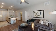 This thoughtfully designed single-floor residence offers a seamless blend of modern aesthetics and functional living. The open-concept living area features rich hardwood-style flooring, a ceiling fan, and large windows dressed with roller shades and floor-to-ceiling curtains that invite generous natural light. The living space comfortably accommodates a full seating arrangement and flows naturally toward the kitchen and dining area.

The kitchen is outfitted with light wood cabinetry extending to the ceiling, stainless steel appliances including a refrigerator, range, and over-the-range microwave, and clean white quartz countertops. A peninsula with bar seating enhances both functionality and social interaction.

The primary bedroom is a calm retreat, highlighted by a stylish barn door leading to a well-organized walk-in closet with built-in drawers, hanging rods, and shelving finished in light natural wood. The en-suite bathroom features a dual-sink vanity with light wood cabinetry, a glass-enclosed shower, wood-look tile flooring, and direct access to the walk-in closet. A second bedroom offers carpet flooring, a large window with outdoor views, and ample space for storage. Throughout the residence, a neutral color palette and contemporary finishes create a cohesive, modern ambiance.