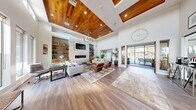 Located in St. George, Utah, this expansive single-floor community clubhouse offers an impressive array of amenities across a generously sized floor plan. The grand entrance welcomes visitors with soaring ceilings, large transom windows flooding the space with natural light, and rich hardwood-style flooring. Two distinct living areas provide versatile gathering spaces — the primary lounge features a dramatic wood-paneled tray ceiling, a modern linear fireplace set against a stone accent wall, built-in shelving, and a statement chandelier, while a secondary lounge area offers floor-to-ceiling windows with panoramic outdoor views and additional built-in cabinetry. A dedicated game room is furnished with a pool table, shuffleboard, a wall-mounted TV, a fireplace, and direct outdoor access. The fully equipped fitness center houses a wide range of cardio machines, free weights, mirrored walls, ceiling fans, and multiple mounted TVs. A tiled steam room provides a spa-like retreat. Additional amenities include a well-appointed communal laundry room with wood-look flooring and a folding station, a vibrant children's activity room, and multiple hallways accented with exposed wood beams and glass partitions, contributing to the space's refined, contemporary character.