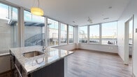 Located at 3100 Chester Ave in Cleveland, Ohio, this modern single-floor unit offers a thoughtfully designed open-concept layout filled with natural light. Expansive floor-to-ceiling windows span multiple rooms, framing urban cityscape views and flooding the interior with daylight throughout the day.

The kitchen is a standout feature, boasting granite countertops, a large central island with an undermount sink, crisp white cabinetry, and black appliances including a gas range and built-in microwave. Track lighting and a pendant fixture illuminate the space, while wood-style flooring flows seamlessly into the open living area.

The bedroom benefits from the same generous window treatment, with granite window sills adding a refined touch and sweeping exterior views creating a bright, airy atmosphere. The bathroom is finished with matching granite countertops, dark cabinetry, a glass-enclosed walk-in shower with white tile surround, and polished concrete flooring, lending a clean, contemporary aesthetic.

Throughout the unit, consistent design elements — including neutral wall tones, wood-look flooring, and modern hardware — create a cohesive and sophisticated ambiance. The unit's position provides elevated outdoor views, making this Cleveland residence a well-appointed and light-filled living space.