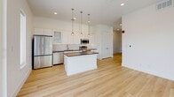 Located at 2217 N Fitzhugh Ave in Dallas, TX 75204, this modern single-floor unit offers a thoughtfully designed open-concept layout that maximizes every inch of its compact footprint. Light hardwood flooring runs throughout the main living area, complementing the bright, neutral walls and creating a clean, cohesive aesthetic.

The kitchen is a standout feature, equipped with sleek white cabinetry extending to the ceiling, dark countertops, a white tile backsplash, and a full suite of stainless steel appliances including a refrigerator, electric range, microwave, and dishwasher. A central island provides additional prep space and serves as a natural focal point, illuminated overhead by a trio of elegant globe pendant lights.

The living area is bathed in natural light through large windows fitted with horizontal blinds, and sliding glass doors open directly onto a private balcony with metal railing, offering pleasant views of the surrounding tree canopy and urban streetscape.

The bathroom is clean and contemporary, featuring large-format white wall tiles, a soaking tub with a combination shower, chrome fixtures, a window for natural light, and gray tile flooring. The overall design of this unit reflects modern urban living with a fresh, minimalist sensibility well-suited for the dynamic Dallas neighborhood it calls home.