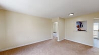 Located at 112 Lawrence St in Middletown, Rhode Island, this single-floor residence offers a clean, functional layout with a warm and neutral aesthetic throughout. The living areas are finished with wall-to-wall carpeting in a soft beige tone, complemented by cream-painted walls and crisp white trim that create a bright, welcoming atmosphere. Natural light flows into the bedrooms through double-hung windows framed by views of surrounding greenery, and baseboard heating units run along the walls to ensure year-round comfort. The kitchen is a practical highlight, featuring rich dark-stained cabinetry with modern hardware, light granite-style countertops, and a full suite of stainless steel appliances including a gas range, built-in microwave, and dishwasher. The bathroom is outfitted with wood-look vinyl flooring, a full tub-and-shower combination with tile surround, a vanity with storage, and a grab bar for added accessibility. The unit's floor plan, as seen in the dollhouse view, reveals a well-organized arrangement of living, sleeping, and kitchen spaces connected by a central corridor, making efficient use of the available footprint. The overall ambiance is clean, move-in ready, and well-maintained.