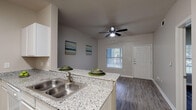 Located at 905 SH-499 Loop S in Harlingen, Texas, this single-floor unit offers a well-designed, open-concept layout that connects the living, dining, and kitchen areas seamlessly. The living and dining space features durable wood-look flooring in a neutral gray tone, crisp white baseboards, and a ceiling fan with integrated lighting — providing both comfort and style. Natural light filters in through windows fitted with horizontal blinds, adding brightness to the neutral gray wall palette throughout.

The kitchen is thoughtfully laid out in a galley style, showcasing granite-look countertops, white cabinetry with ample upper and lower storage, a double stainless steel sink, and white appliances including a refrigerator, electric range, and microwave. A breakfast bar peninsula opens the kitchen toward the dining area, enhancing the sense of flow and connectivity.

The bedroom offers a comfortable, quiet retreat with continued wood-look flooring, a window with blinds for natural light, and direct access to the hallway. The bathroom is clean and functional, featuring a full tub and shower combo with white tile surround, wood-look flooring, and efficient use of space. Throughout the unit, the consistent flooring, neutral tones, and clean finishes create a cohesive and inviting atmosphere.