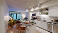 This contemporary 2-bedroom, 2-bathroom residence at 816 Portland Ave in Minneapolis showcases an industrial-modern aesthetic defined by exposed concrete ceilings, light hardwood flooring, and large windows that draw in natural light throughout. The open-concept kitchen and living area serves as the heart of the home, featuring a well-appointed kitchen with white cabinetry, subway tile backsplash, stainless steel appliances, and a spacious island with grey quartz countertops — ideal for cooking and entertaining. Pendant lighting adds a stylish focal point above the island. The adjoining living room offers access to an outdoor balcony through floor-to-ceiling sliding glass doors, framing views of the surrounding cityscape. The primary bedroom is a comfortable retreat with warm ambient lighting and bold wall art, while the second bedroom features an exposed concrete accent wall and large windows with urban views. Both bathrooms are finished in a clean, modern style with white vanities, ample drawer storage, and large mirrors. A hallway and dedicated closet provide practical storage. The overall ambiance is urban and refined, blending raw architectural elements with polished finishes for a cohesive, contemporary living experience in the heart of Minneapolis.