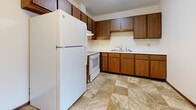 Located at 332 Cypress Drive in Saint Joseph, Minnesota, this single-floor unit offers a practical and well-organized layout suited for comfortable everyday living. The living area is generously sized, featuring neutral-toned carpet underfoot, cream-colored walls, and a large picture window framed in warm wood trim that allows natural light to fill the space. A wall-mounted air conditioning unit and baseboard heating ensure year-round climate control.

The kitchen is equipped with rich wood cabinetry extending to the upper and lower walls, offering ample storage and counter space. White appliances, including a refrigerator and range, complement the cabinetry, while durable tile flooring adds practicality to the space.

The unit includes multiple carpeted bedrooms, each with cream-painted walls and dark wood trim baseboards. One bedroom features a large window overlooking greenery outside, while another offers a quieter, more private setting. Both rooms include closet access.

The bathroom is finished with neutral stone-look tile flooring, a single-sink vanity with wood cabinetry beneath, a toilet, and a full tub and shower combination. The space transitions smoothly between rooms through dark wood-trimmed doorways, maintaining a cohesive and functional design throughout the unit.