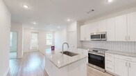 Located at 2652 S Main St NW in Kennesaw, GA, this thoughtfully designed single-floor, one-bedroom, one-bathroom residence offers a clean, contemporary aesthetic throughout. The open-concept kitchen serves as the heart of the home, showcasing a granite-topped center island with an undermount sink, crisp white shaker cabinetry, a tile backsplash, and a full suite of stainless steel appliances including a refrigerator with ice maker, electric range, and over-the-range microwave. Light wood-style flooring flows seamlessly through the kitchen and living areas, lending warmth and continuity to the space. The living area benefits from natural light provided by windows fitted with blinds and direct access via a glass-panel door. The bedroom is a calm retreat featuring plush carpeting, a ceiling fan, and a window with outdoor views. A walk-in closet with wire shelving provides ample storage. The full bathroom is well-appointed with a double granite-topped vanity, white cabinetry, a large wall mirror, and a tiled tub-shower combination. A stacked washer and dryer unit is conveniently integrated within the bathroom area. Recessed lighting throughout enhances the bright, modern ambiance of this well-appointed Kennesaw residence.