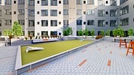 Located at 340 S Market St in Wilmington, Delaware, this expansive outdoor courtyard is nestled within a contemporary multi-story building complex featuring a modern architectural design with contrasting gray and white paneled facades, large windows, and clean geometric lines. The courtyard's ground level is paved with a patterned brick layout, incorporating terracotta accent strips that add visual interest and define distinct activity zones throughout the space.

The courtyard offers a variety of recreational amenities. A full-length bocce ball court anchors one section of the space, bordered by casual lounge seating. Nearby, a life-sized chess set is inlaid into the paved surface, providing an engaging feature for visitors. Bistro-height tables and chairs in bold orange and red tones are scattered throughout, creating informal gathering spots.

Thoughtfully designed raised planters line the perimeter, filled with bamboo trees, ornamental grasses, and decorative stone, providing a natural buffer and a touch of greenery against the urban backdrop. Benches are positioned near the planting beds for quiet relaxation. The open-air design allows abundant natural light to flood the courtyard, creating a bright and welcoming atmosphere. The overall ambiance is modern, communal, and well-appointed, making it a functional and attractive outdoor amenity space.