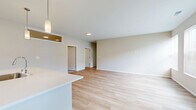 This well-appointed 2-bedroom, 2-bathroom single-story home offers a generous and thoughtfully designed floor plan. The open-concept kitchen and living area serves as the heart of the home, featuring light hardwood flooring that flows throughout the main living spaces. The kitchen is outfitted with white shaker-style cabinetry extending to the ceiling, a classic subway tile backsplash, stainless steel appliances including a refrigerator, electric range, and microwave, and a large island with a quartz countertop and undermount sink — ideal for both cooking and casual dining. Pendant lighting accents the island, adding a modern touch. The living room is bright and open, with large windows that invite natural light and views of the surrounding greenery. The primary bedroom is a comfortable retreat, featuring plush carpeting, access to a private en-suite bathroom with a walk-in shower, white vanity cabinetry, and built-in shelving. A spacious walk-in closet with wire shelving provides ample storage. The second bedroom and additional full bathroom offer flexibility for guests or a home office. An attached garage with a concrete floor provides secure parking and additional storage. The exterior features a well-maintained driveway and landscaped surroundings.