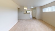 This single-floor residence offers a well-organized layout that balances comfort and functionality throughout. The living room serves as the central gathering space, featuring soft wall-to-wall carpeting, a tiled fireplace as a focal point, and a sliding glass door that opens to an outdoor patio, allowing natural light and outdoor views to fill the room. A clerestory-style window above adds additional brightness to the space.

Adjacent to the living area, the galley-style kitchen is efficiently designed with white cabinetry, stone-look tile flooring, laminate countertops, and stainless steel appliances including a refrigerator and range with overhead ventilation. A double-basin sink and dishwasher provide practical utility, while a pass-through counter connects the kitchen to the dining or entry area.

The bedroom is a quiet, carpeted retreat illuminated by a large window fitted with vertical blinds, offering views of surrounding greenery. Baseboard heating ensures year-round comfort. The room is conveniently connected to a bathroom and a walk-in closet area. The bathrooms feature warm-toned tile flooring, grab bars for added accessibility, and clean, neutral finishes throughout. An additional room with wide windows and baseboard heating provides flexible use as a second bedroom or office.