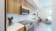 Located at 11100 Main St in Bellevue, WA, this thoughtfully designed one-bedroom, one-bathroom residence makes excellent use of its compact footprint. The open layout connects the kitchen, dining, and living areas seamlessly, creating a cohesive and functional living space. The galley-style kitchen is outfitted with warm wood cabinetry extending to the ceiling, stainless steel appliances including a smooth-top range and over-the-range microwave, a white quartz countertop, and a striking geometric white tile backsplash that adds visual texture. Light hardwood-style flooring runs throughout, tying the space together. The living area benefits from abundant natural light streaming through large sliding glass doors that open to a private balcony with views of the surrounding greenery. The bedroom is a calm, well-proportioned retreat with high ceilings, open closet storage, and a sliding door that also connects to the outdoor balcony. The bathroom features a warm wood vanity with a white countertop, a large mirror, and a glass-enclosed shower, all set against clean white walls and light tile flooring. Throughout, the unit maintains a crisp, modern aesthetic with a neutral palette that feels both airy and polished.