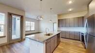 This well-appointed 3-bedroom, 2-bathroom residence is designed with a modern aesthetic and thoughtful layout across a single floor. The open-concept kitchen and living area serves as the heart of the home, featuring a large center island with granite countertops, an undermount sink, and stylish pendant lighting. Taupe cabinetry with brushed hardware, a tile backsplash, and a full suite of stainless steel appliances — including a refrigerator, range, and microwave — complete the kitchen. Wood-style plank flooring flows seamlessly throughout the entire residence, lending warmth and continuity to every room. The living area receives natural light through large windows with views of the surrounding community, and a ceiling fan adds comfort to the space. Each of the three bedrooms is well-sized, with the primary bedroom offering generous proportions, a ceiling fan, and ample natural light. Three closets provide abundant storage throughout the unit. Both bathrooms mirror the home's refined finishes, featuring granite-topped vanities with undermount sinks, full soaking tubs with tiled surrounds, and wood-style flooring. A hallway connects the private bedroom wing to the main living areas, creating a functional and cohesive floor plan.