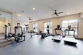 Located at 2000 James Jackson Pkwy in Atlanta, GA, this well-appointed fitness center offers a spacious, single-floor layout designed to support a comprehensive workout experience. The facility is generously sized, providing ample room for a diverse array of exercise equipment without feeling overcrowded.

The cardio zone features multiple treadmills, elliptical trainers, rowing machines, and a stationary spin bike, all positioned along a wall of large, black-framed windows that flood the space with natural light and offer views of an outdoor pool area and surrounding greenery. This bright, open atmosphere creates an inviting environment for exercise.

The strength training area is equally well-equipped, housing a power rack with barbell and weight plates, a cable machine, a multi-functional cable cross system, and various selectorized strength machines. A dedicated free weights section includes a full rack of dumbbells paired with an adjustable bench, supported by wall mirrors that enhance the sense of depth throughout the space.

Structural columns divide the floor plan into distinct workout zones while maintaining an open, cohesive feel. Multiple ceiling fans are mounted throughout, ensuring consistent airflow and comfort. Recessed lighting supplements the natural light, keeping the space bright and functional. Durable rubber and carpet flooring underfoot provide both safety and comfort during training sessions.