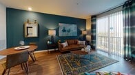 Located at 21 Executive Dr in Stoneham, Massachusetts, this single-floor residence offers a thoughtfully designed layout with modern finishes and a cohesive, vibrant aesthetic. Warm hardwood-style flooring runs throughout the unit, complementing the contemporary design at every turn.

The open-concept living and dining area serves as the heart of the home, anchored by a bold teal accent wall adorned with abstract artwork. Large sliding glass doors with vertical blinds and patterned drapes flood the space with natural light while providing access to an outdoor area. The living room accommodates comfortable seating and stylish accent furnishings, while a round dining table sits nearby for convenient everyday use.

The kitchen is well-equipped with a full suite of stainless steel appliances, including a refrigerator, range, built-in microwave, and dishwasher. Gray shaker-style cabinetry with ample storage, white quartz countertops, and a herringbone tile backsplash complete the polished look.

The bedroom features a soothing teal accent wall, generous natural light from a large window with outdoor views, and direct access to a walk-in closet. The bathroom is outfitted with a wide vanity, framed mirror, and hardwood-style flooring, maintaining the refined character found throughout the residence.