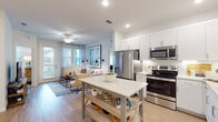 This well-appointed single-floor residence offers a thoughtfully designed open-concept layout that seamlessly connects the kitchen and living areas. The kitchen is a standout feature, showcasing white shaker cabinetry extending to the ceiling, a white subway tile backsplash, stone countertops, a full suite of stainless steel appliances, and recessed lighting. An island provides additional prep space and casual dining potential.

The living area flows naturally from the kitchen, bathed in natural light from large windows and a glass door that opens to an outdoor balcony. Warm hardwood-style flooring runs throughout the main areas, complemented by ceiling fans and soft neutral wall tones.

The primary bedroom is carpeted and generously sized, featuring multiple windows and an en suite bathroom with a glass-enclosed walk-in shower, a white vanity with stone countertops, hardwood-style flooring, and direct access to a walk-in closet. A second bedroom offers similar comfort and natural light. The second bathroom includes a full soaking tub and shower combination with a matching white vanity. A dedicated in-unit laundry room with full-size washer and dryer and built-in shelving rounds out the space.