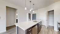 This single-floor residence showcases a contemporary open-concept design that seamlessly connects the kitchen, dining, and living areas. The kitchen serves as the centerpiece, featuring a large island with quartz countertops, an undermount sink, and pendant lighting suspended above. Dark espresso-toned cabinetry provides strong visual contrast against the light countertops, while a full suite of stainless steel appliances—including a refrigerator, range, microwave, and dishwasher—rounds out the functional workspace.

The living area extends naturally from the kitchen, finished with wood-look luxury vinyl plank flooring and a ceiling fan overhead. A sliding glass door leads to a balcony offering outdoor views, allowing natural light to fill the space. A wall-mounted mini-split unit and baseboard heating provide climate control throughout.

The bedroom is carpeted for comfort, features a ceiling fan, and is served by a walk-in closet with wire shelving for organized storage. The bathroom includes dark cabinetry with a white countertop vanity, a large mirror with overhead lighting, and a full tub-shower combination. Light vinyl plank flooring completes the clean, neutral aesthetic throughout the wet areas.